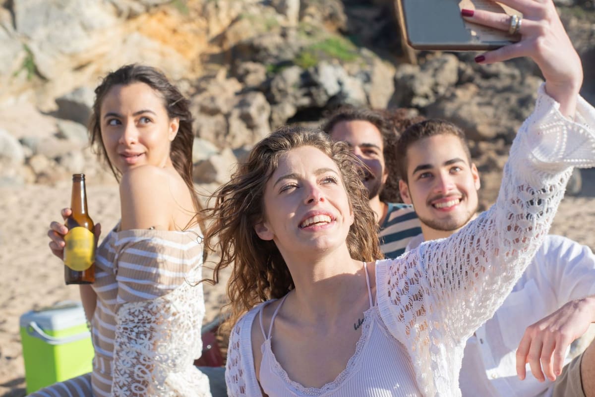 Four friends on a beach, one holding a phone up for a group selfie