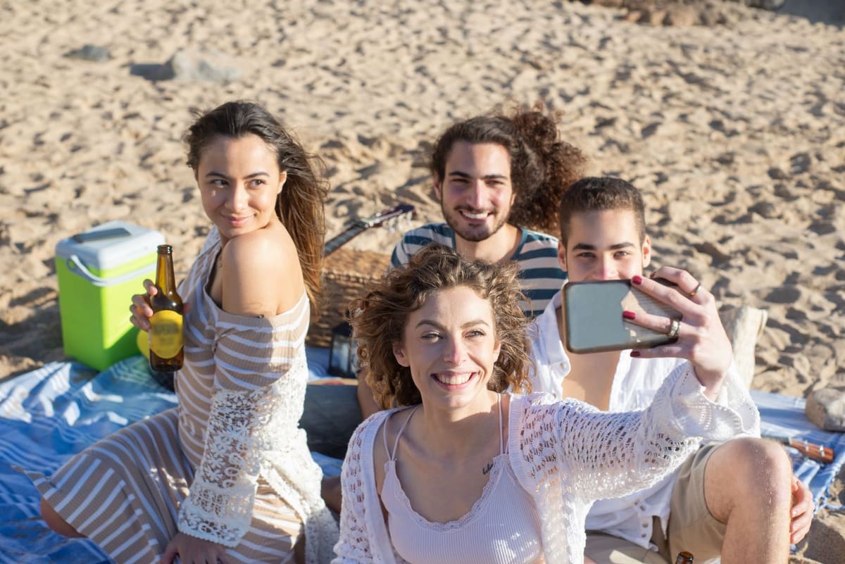 Friends on a beach picnic, leaning in for a selfie