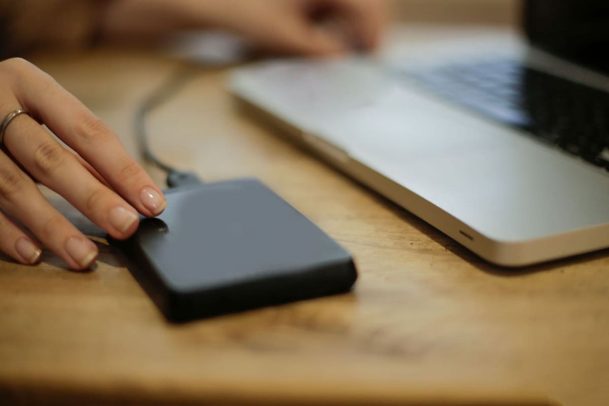 A hand plugging a small external drive into a laptop