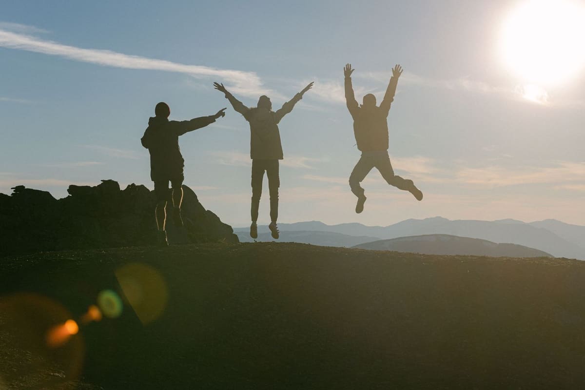Three friends jumping in silhouette on a mountain top at sunset